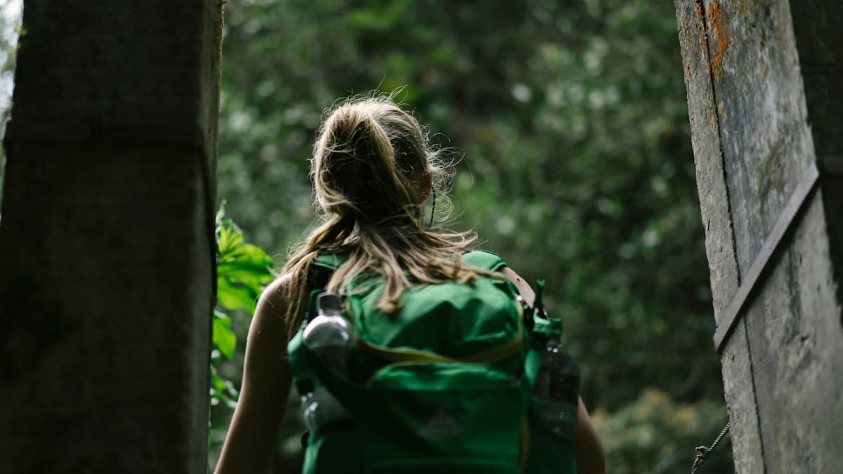 Una viajera con mochila verde recorre un sendero entre árboles en Cocora